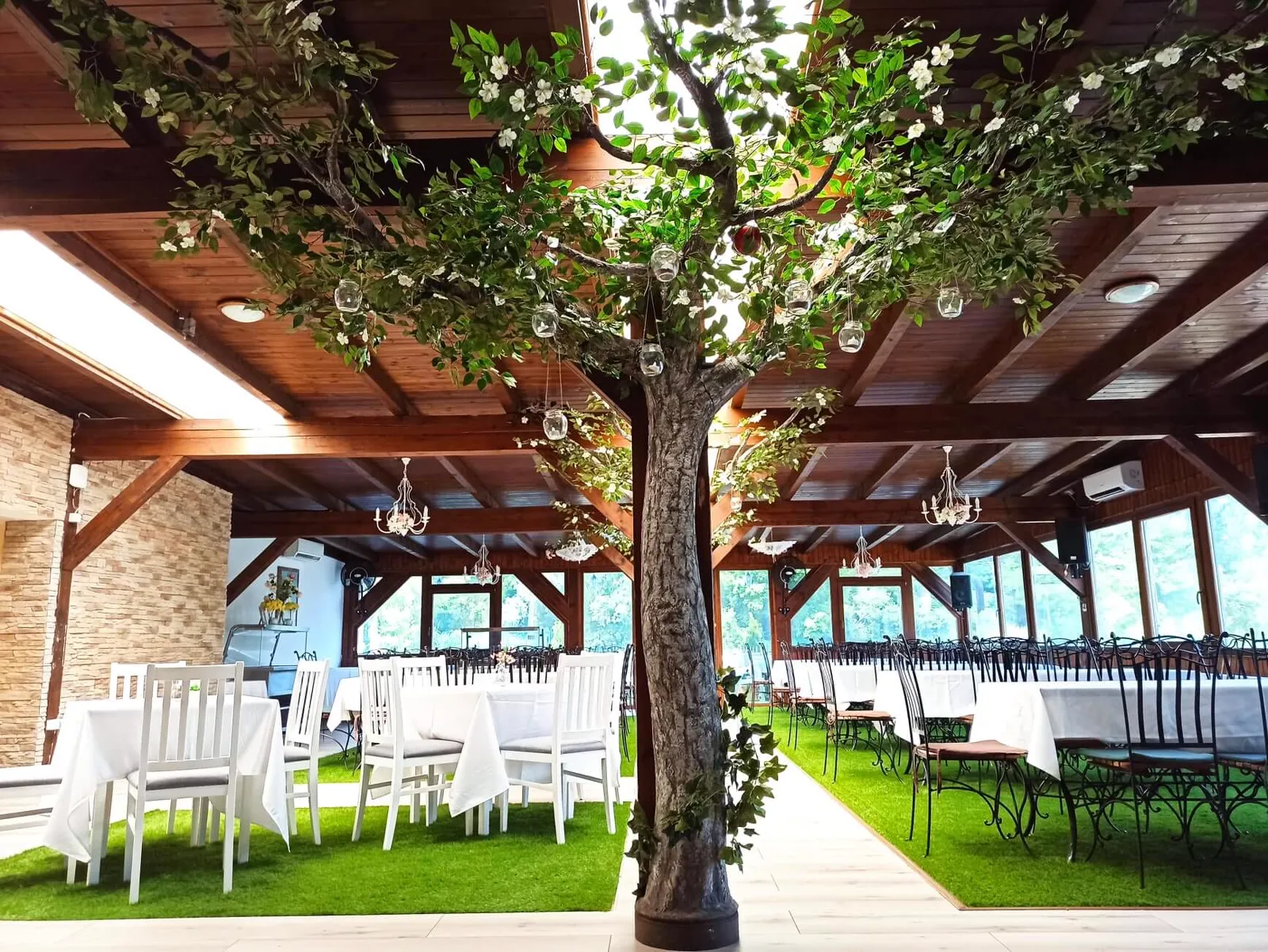 Megterített kerek asztalok a beltéri fa körül, függő üvegdíszekkel